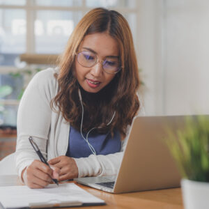 Asian people study online course via internet. Young girl watching business lesson from laptop computer and note lecture to notebook at home.